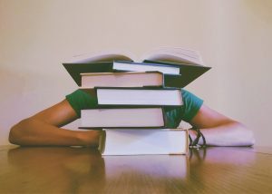 Person studying with head down behind a large pile of books.